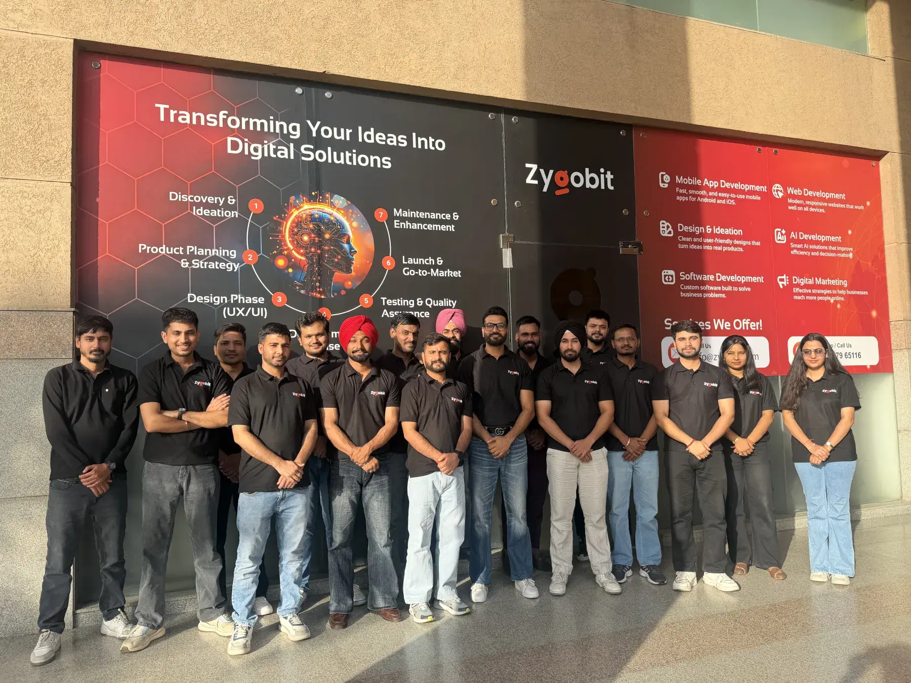 The Zygobit team gathered in front of the company's branded services wall at the Mohali, India headquarters